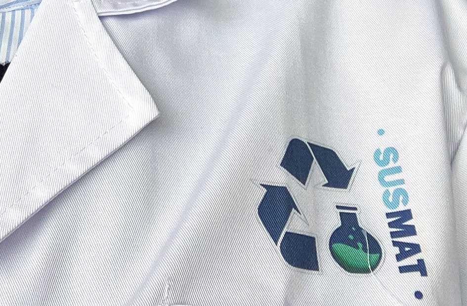 The SusMatLab logo, recycling arrows and a flask, printed on a lab coat